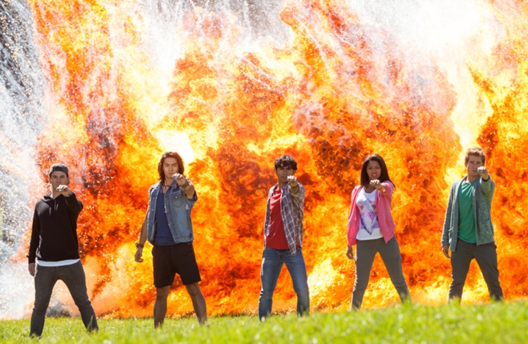 Five Power Rangers standing in front of explosion of fire