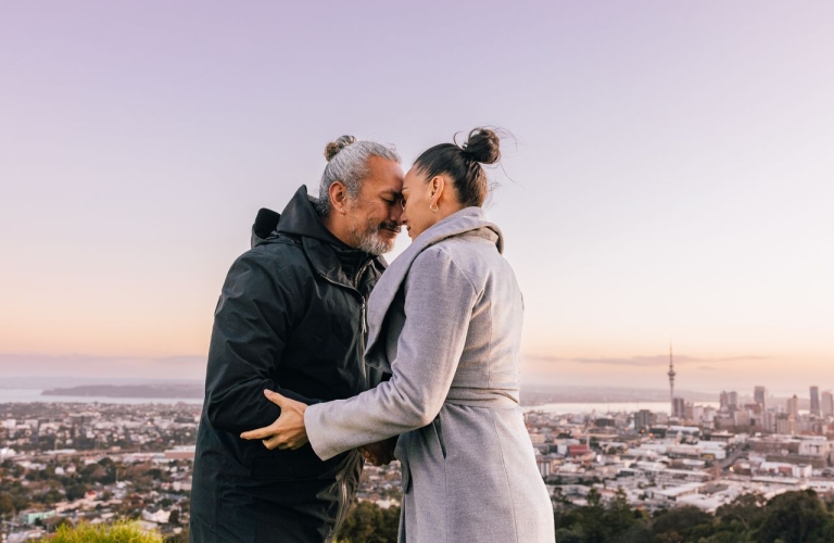 A man and woman sharing a hongi overlooking Auckland city at sunrise.