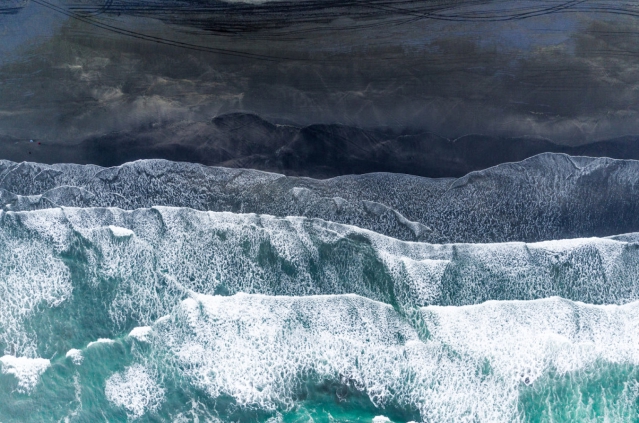 Bird's eye view of waves crashing on black sand beach